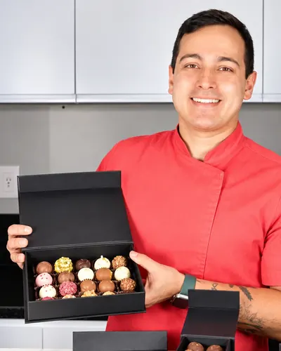 Gustavo Ono, de dólmã vermelha, sorrindo e segurando uma caixa de trufas